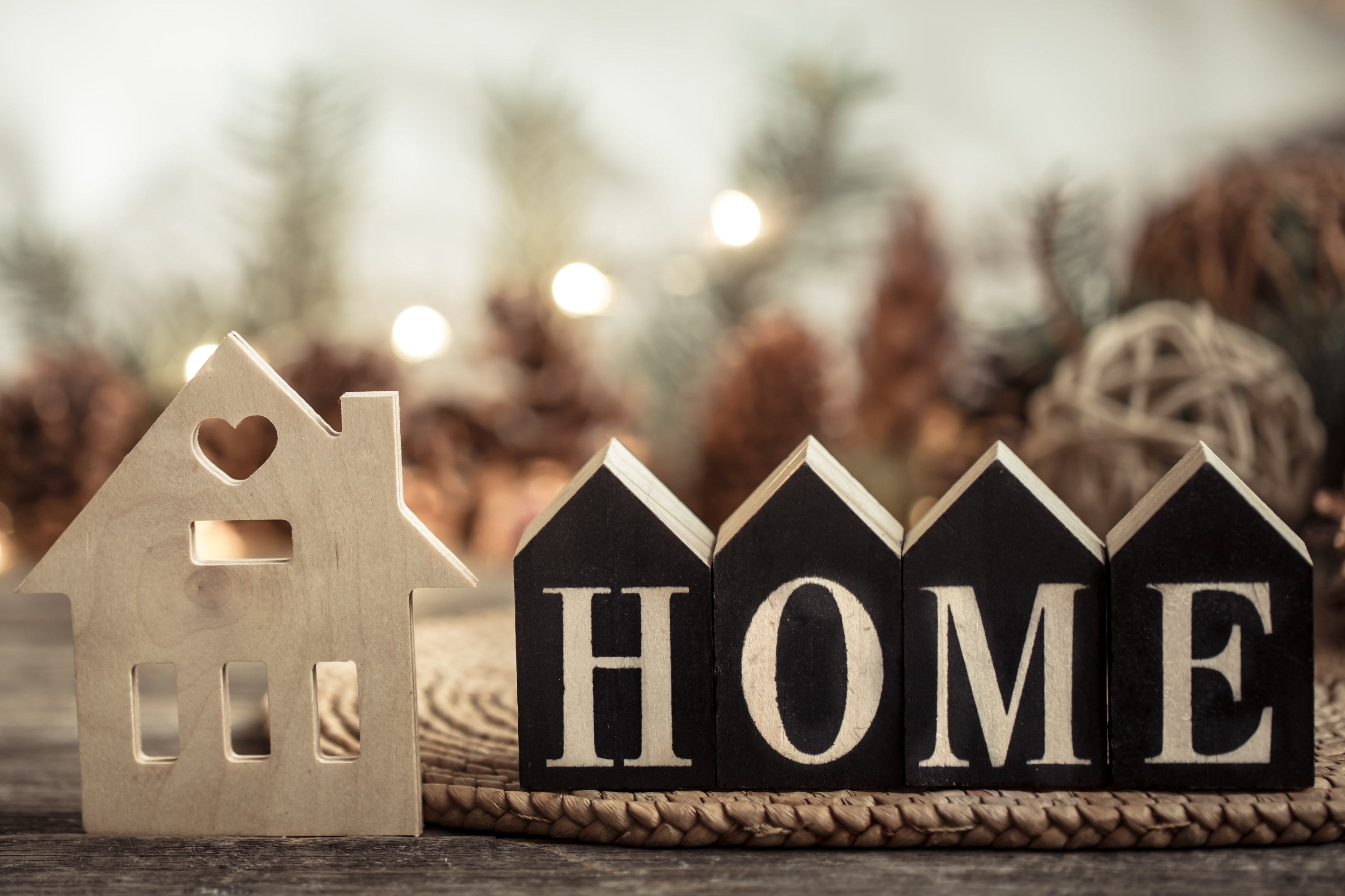 picture depicting the word home, with a small wooden figurine house beside.Blurred background.