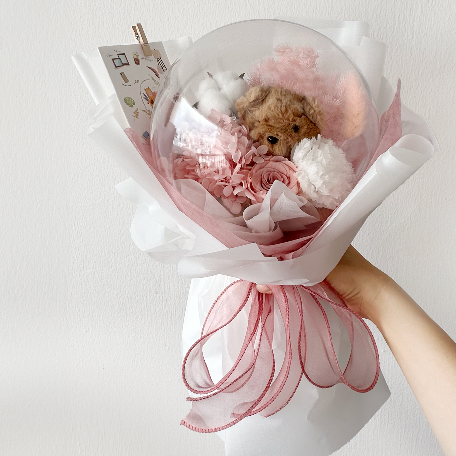 Pink teddy bear with flower bouquet.