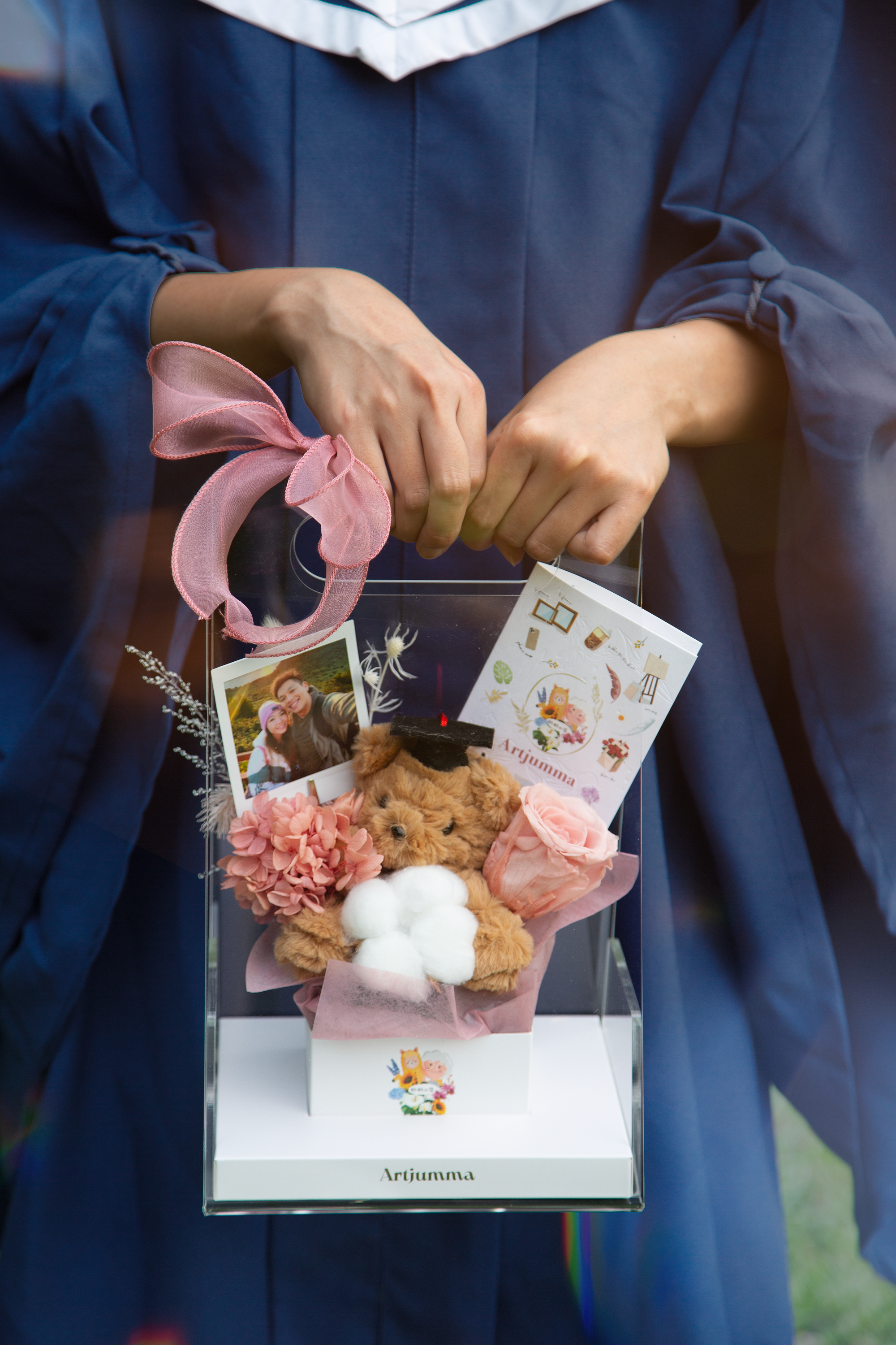 Girl's hands holding graduation teddy bear and preserved purple flowers gift box with purple ribbon